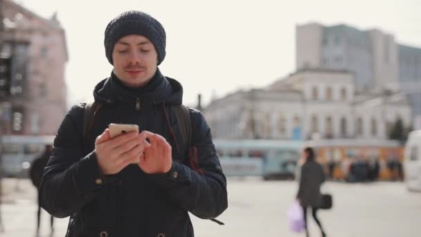 Hombre utiliza teléfono inteligente caminando en una calle de la ciudad — Vídeos de Stock