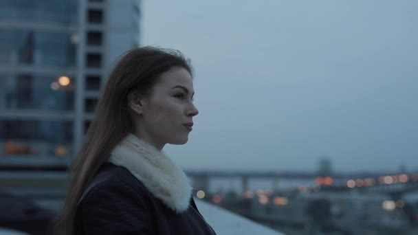 Jonge vrouw kijkt uit naar de avond city scape — Stockvideo