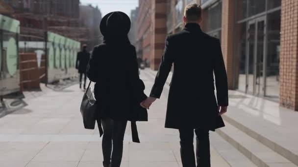 Stylish couple walking along city street holding hands, rear view — Stock Video