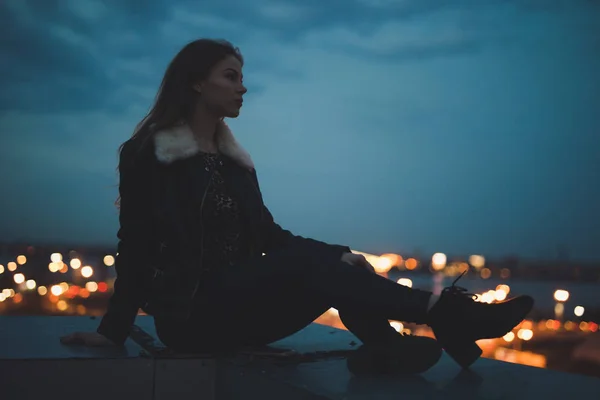 Silhouette einer allein auf dem Dach sitzenden Frau, Stadt im Hintergrund — Stockfoto