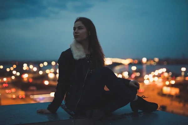 Silueta de mujer sola sentada en el techo, ciudad en el fondo —  Fotos de Stock