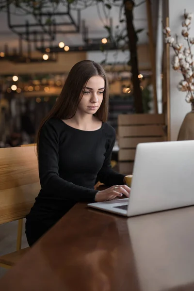 坐在咖啡馆里的用笔记本电脑工作的妇女 — 图库照片
