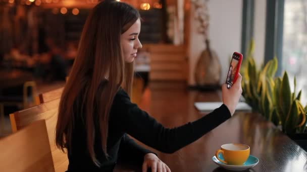 Женщина делает селфи на смартфоне, сидя в кафе — стоковое видео