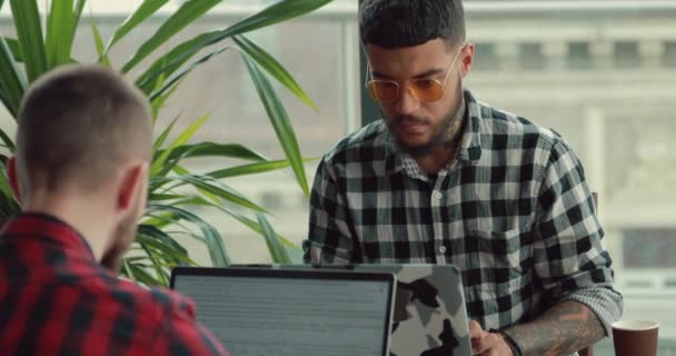 Молоді чоловіки фотографи ведуть блог онлайн, працюючи на ноутбуках комп'ютерів в кафе — стокове відео