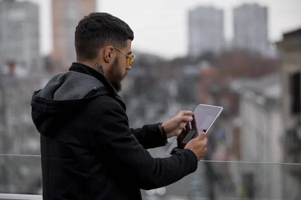 Молодий стильний чоловік читає книгу тримає планшетний ПК в місті — стокове фото