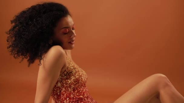 Красивая женщина позирует в студии на оранжевом фоне — стоковое видео