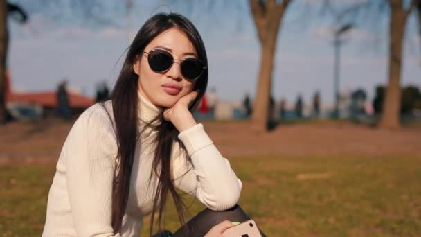 Asiatique femme assis dans un parc avec des lunettes — Video