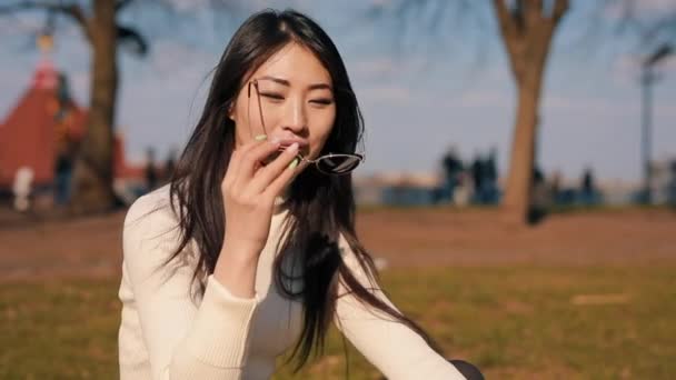 Mujer asiática sentada en un parque con gafas — Vídeo de stock