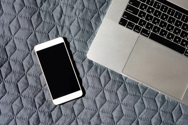 Pantalla de teléfono inteligente en blanco cerca del teclado portátil en la cama — Foto de Stock