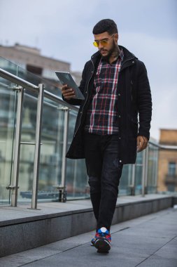 Genç ve şık bir adam elinde tabletle şehirde yürüyor.