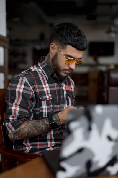 Стильний чоловік у картатій сорочці за допомогою смартфона, що сидить у кафе — стокове фото