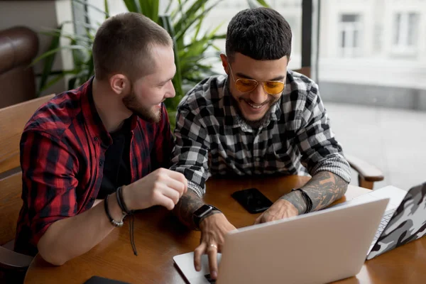 Young men friends laughing looking at laptop monitor