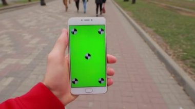 Pov, şehir sokakta yürüyen bir erkek elinde akıllı telefon boş yeşil ekran
