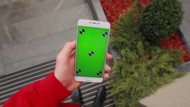 Eerste persoon weergave, blanco groen scherm van smartphone in een mannelijke hand op stad — Stockvideo