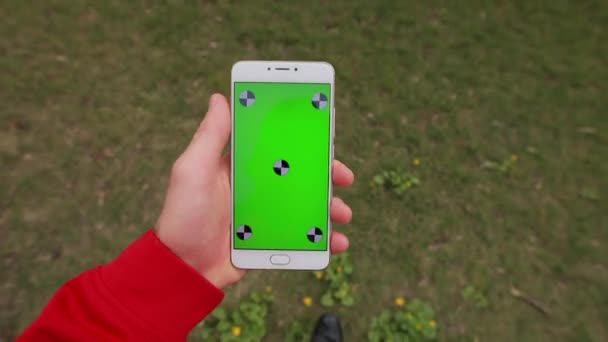 1e persoon weergave, blanco groen scherm van smartphone in een mannelijke hand wandelen op een gras — Stockvideo