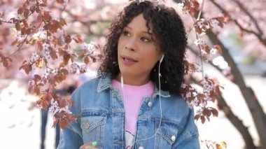 Parkta müzik dinleyen bir kadın, etrafta kiraz ağaçları...