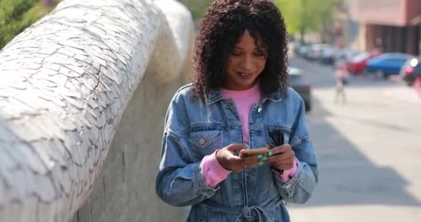 Мультирасовая женщина читает сообщения по телефону со смехом в городе — стоковое видео