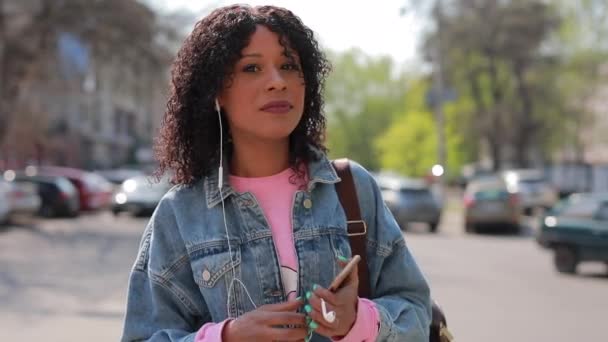Mångrasistisk kvinna lyssnar på musik i en stad på våren — Stockvideo