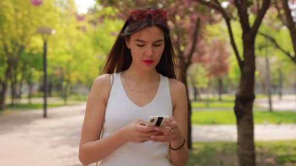 夏の公園を歩くスマートフォンでメッセージを読む女性 — ストック動画