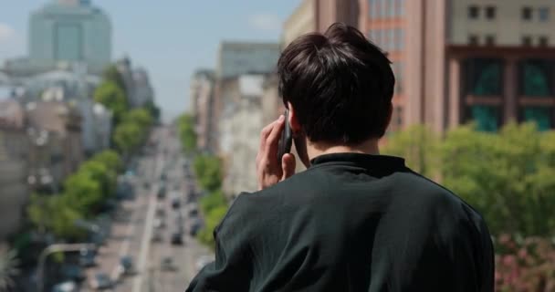 Человек с заднего вида разговаривает по смартфону в городе — стоковое видео
