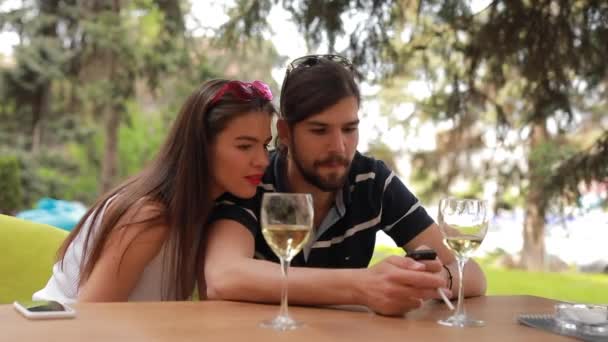 Пара побачень, чоловік і жінка виглядають щось в смартфоні, сидячи за столом — стокове відео
