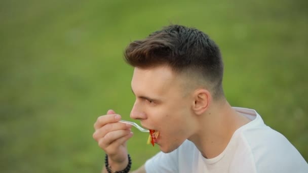Çimenlerin üzerinde oturan salata yiyen adam — Stok video