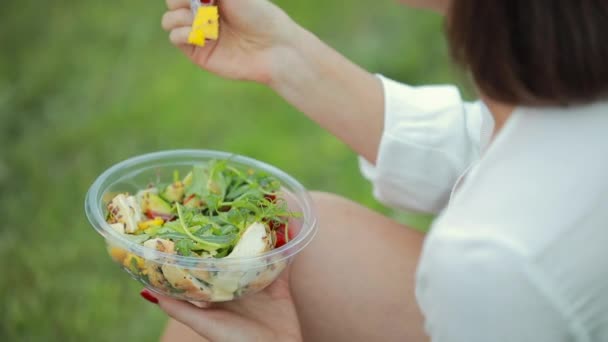 Vrouw eet salade zittend op gras — Stockvideo