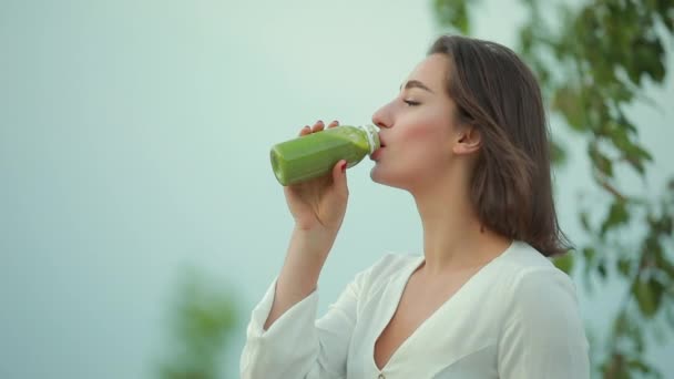 Hermosa mujer bebiendo batido verde al aire libre — Vídeos de Stock