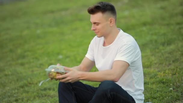 Hombre mezclando ensalada sentado en la hierba — Vídeos de Stock