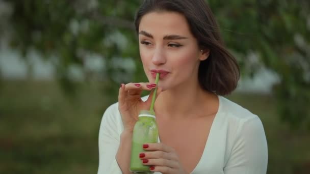 Hermosa mujer bebiendo batido verde al aire libre, concepto de desintoxicación — Vídeos de Stock