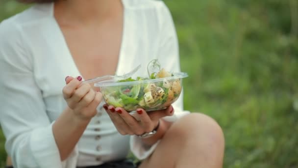 Belle femme mangeant de la salade assise sur l'herbe — Video