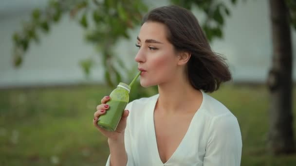 Красивая женщина пьет зеленый смузи на открытом воздухе — стоковое видео