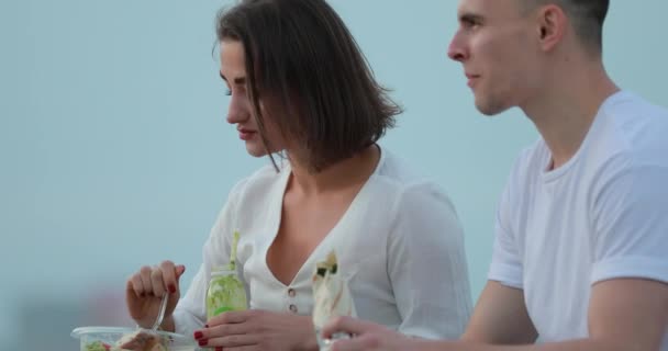 Pareja joven comiendo ensalada sentado en el terraplén de la ciudad — Vídeo de stock