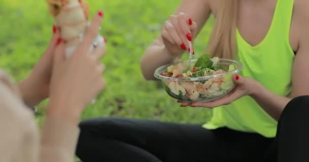 Mujeres de fitness comiendo ensalada fresca en un parque, comida vegetariana saludable — Vídeos de Stock