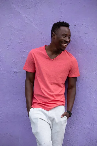 Усміхнений афроамериканець людина модель постановки в порожній життя коралові футболки біля фіолетових стін — стокове фото