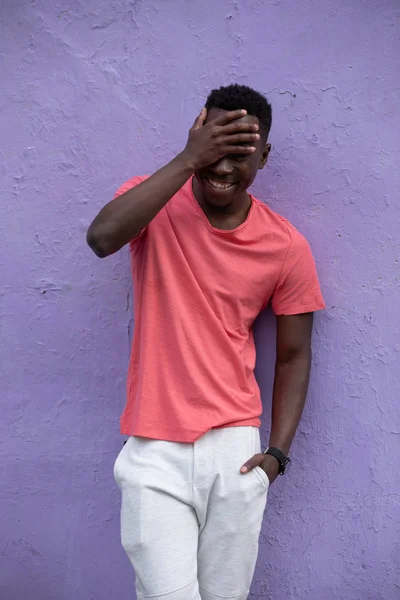 Smiling African American man model posing in empty living coral t-shirt near violet wall — Stock Photo, Image