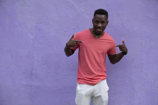 Modelo de hombre afroamericano posando en una camiseta de coral viva vacía en la pared violeta — Foto de Stock