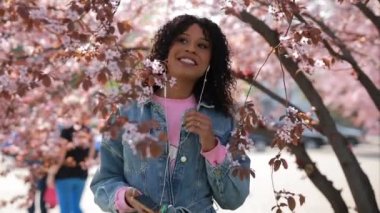 Çok ırklı kadın bir parkta müzik dinlerken, kiraz çiçekleri ağaç etrafında