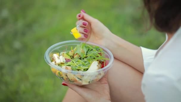 Vrouw eet salade zittend op gras — Stockvideo