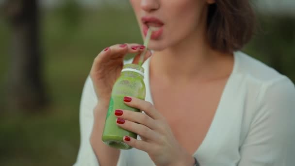 Cultivé femme méconnaissable boire smoothie vert en plein air avec de la paille — Video