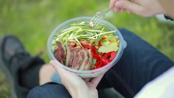 Man eating salad sitting on grass — Stock Video