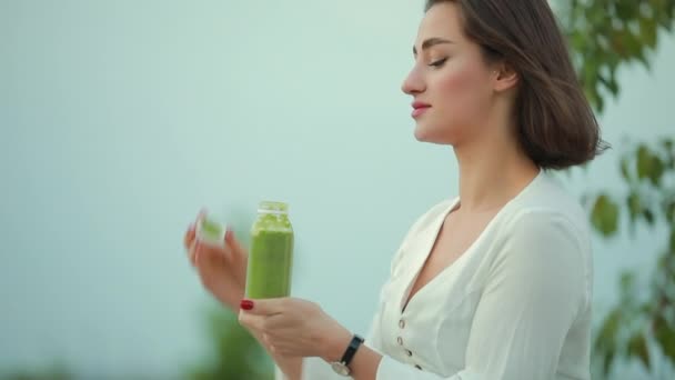 सुंदर महिला पिण्याचे हिरव्या स्मोथी मैदानी — स्टॉक व्हिडिओ