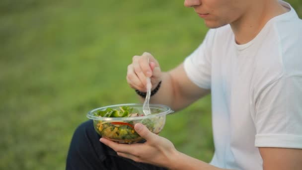 Человек ест салат сидя на траве — стоковое видео
