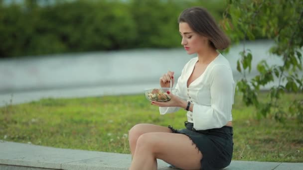 Mooie vrouw eet salade zittend in een park — Stockvideo