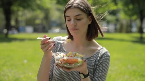 Kobieta jedząca świeżą sałatkę siedzącą w letnim parku — Wideo stockowe