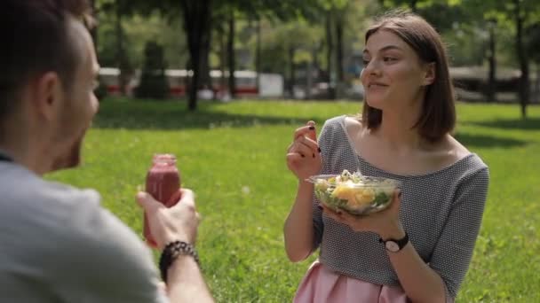 Pareja vegetariana joven comiendo ensalada y bebiendo batido en un parque — Vídeos de Stock