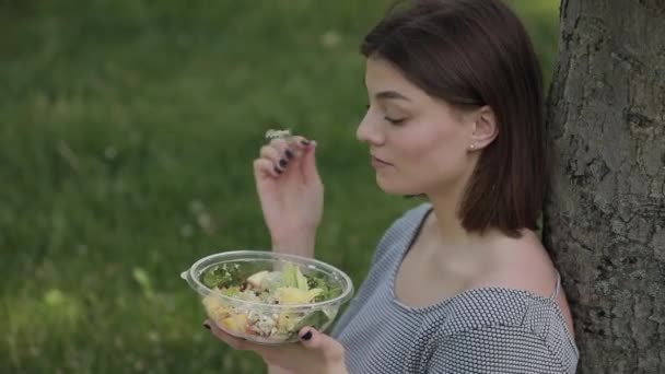 여름 공원에 앉아 신선한 샐러드를 먹는 여자 — 비디오