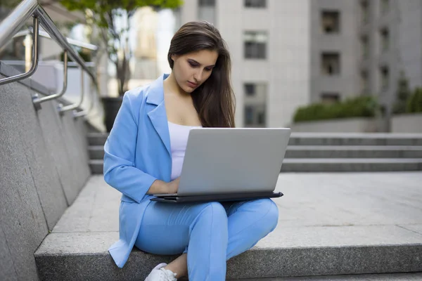 Businesswoman working by laptop PC outdoor near building