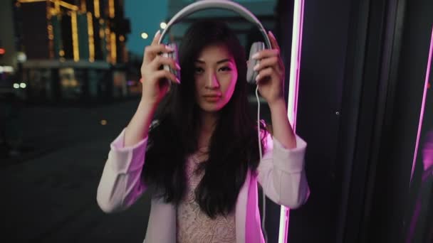Ásia mulher coloca no fone de ouvido no noite cidade — Vídeo de Stock