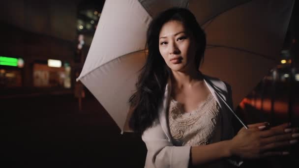 Азиатка крутит зонтик в ночном городе — стоковое видео